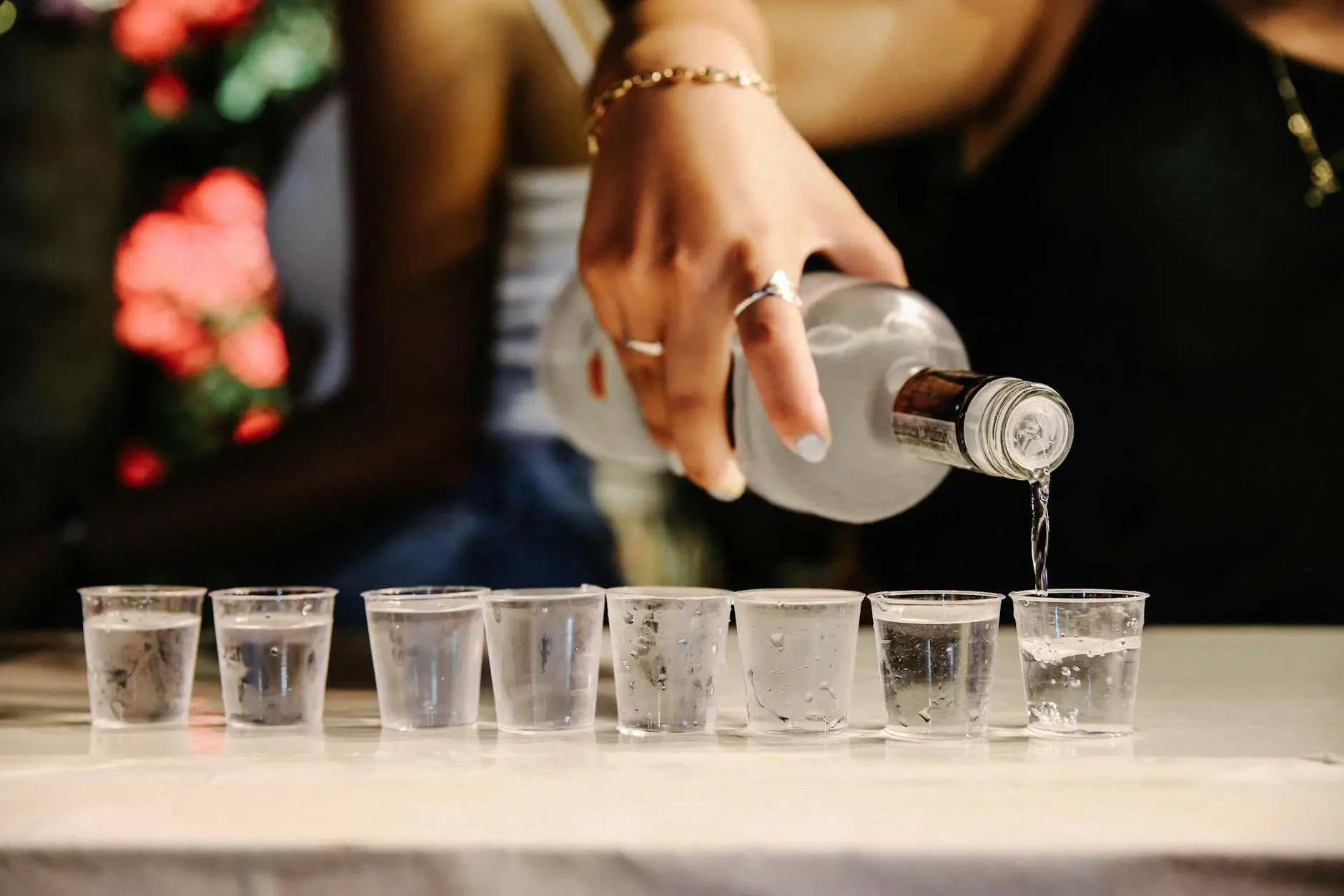Close-up of a woman pouring vodka into shot glasses during a festive party setting.