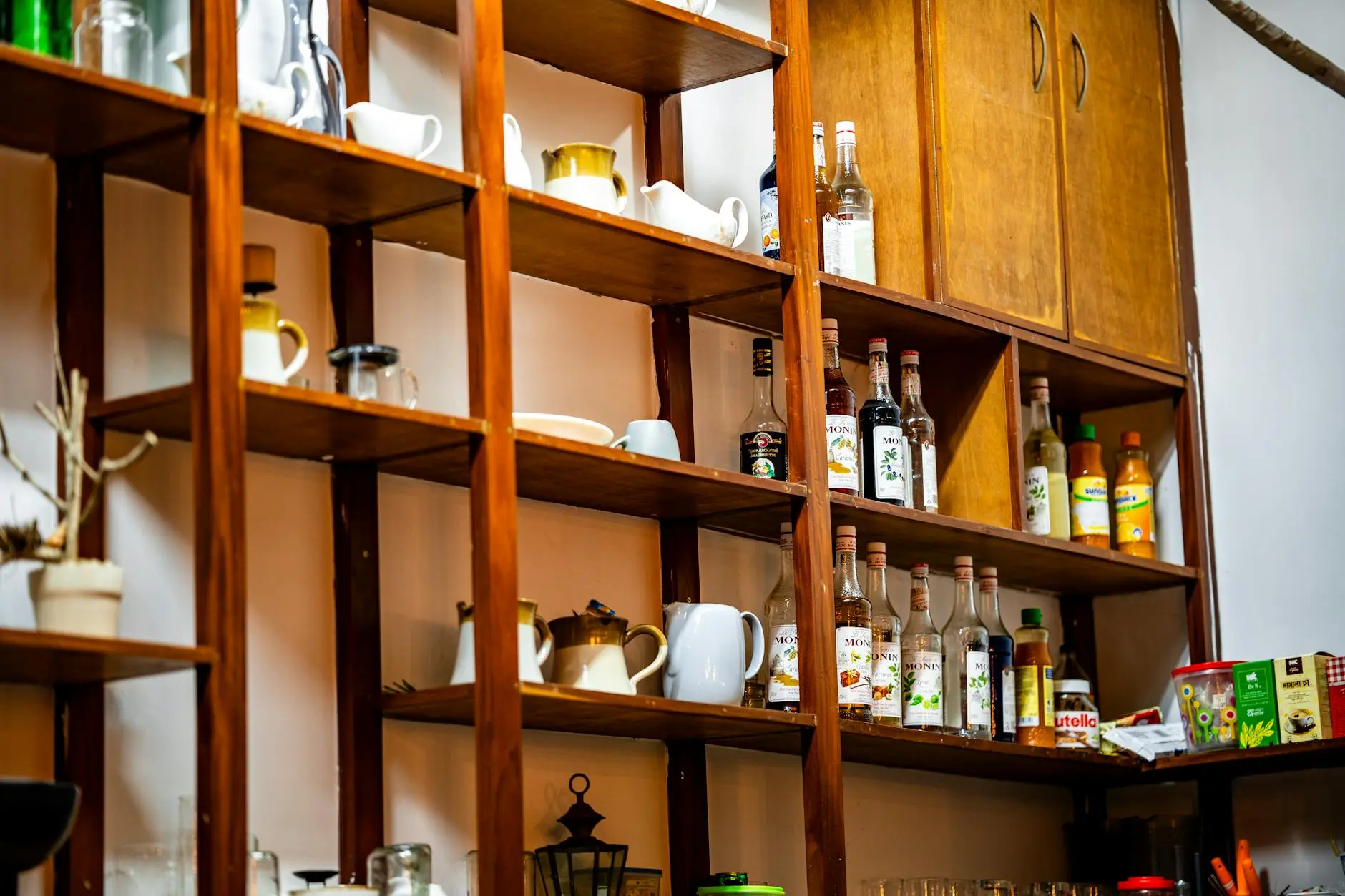 A well-organized café shelf with assorted bottles and mugs, highlighting interior design elements.